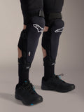 Alpinestars A-Impact Plasma Pro kniebeschermers, zwart en wit, met Nucleon PLASMA-technologie branding, gedragen met zwarte sokken en zwarte mountainbikeschoenen, stevige klittenbandsluitingen, ergonomische beschermingsuitrusting voor off-road fietsen