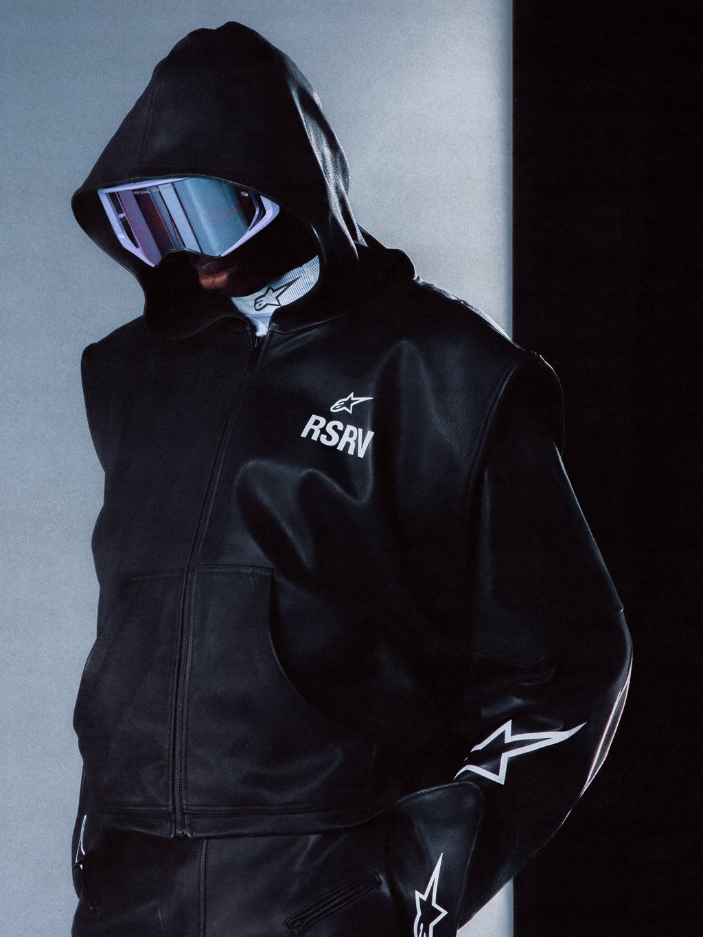 Alpinestars RSRV Axis Leather Hoodie, veste à capuche en cuir noir avec logo RSRV et étoile, manches ornées d'étoiles blanches, fermeture éclair, style urbain futuriste premium