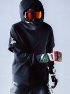 Alpinestars RSRV Vault Hoodie, sweat à capuche noir pour homme, style urbain motorsport, porté avec casque et lunettes réfléchissantes orange, logos blancs sur la manche, look streetwear premium