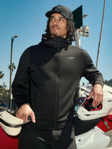 Alpinestars Cypher Hoodie, zwarte lifestyle fleece met rits, hoge capuchon met branding, klein wit Astars-logo op de borst, gedragen met een zwarte pet door een rijder die een witte motorcrosshelm vasthoudt, casual motorsport streetwear