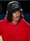 Man met Alpinestars Intuitive Snapback pet in het zwart, voorzien van een gestructureerde kroon en 'Racing Ahead' logo-borduurpatch, gecombineerd met een felrode hoodie, casual lifestyle streetwear