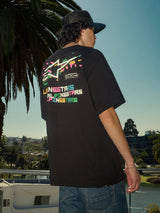 Alpinestars Wild Oversized CSF Tee, t-shirt à manches courtes noir, logo Astars multicolore éclatant au dos, coupe surdimensionnée, photo lifestyle streetwear décontractée avec des palmiers