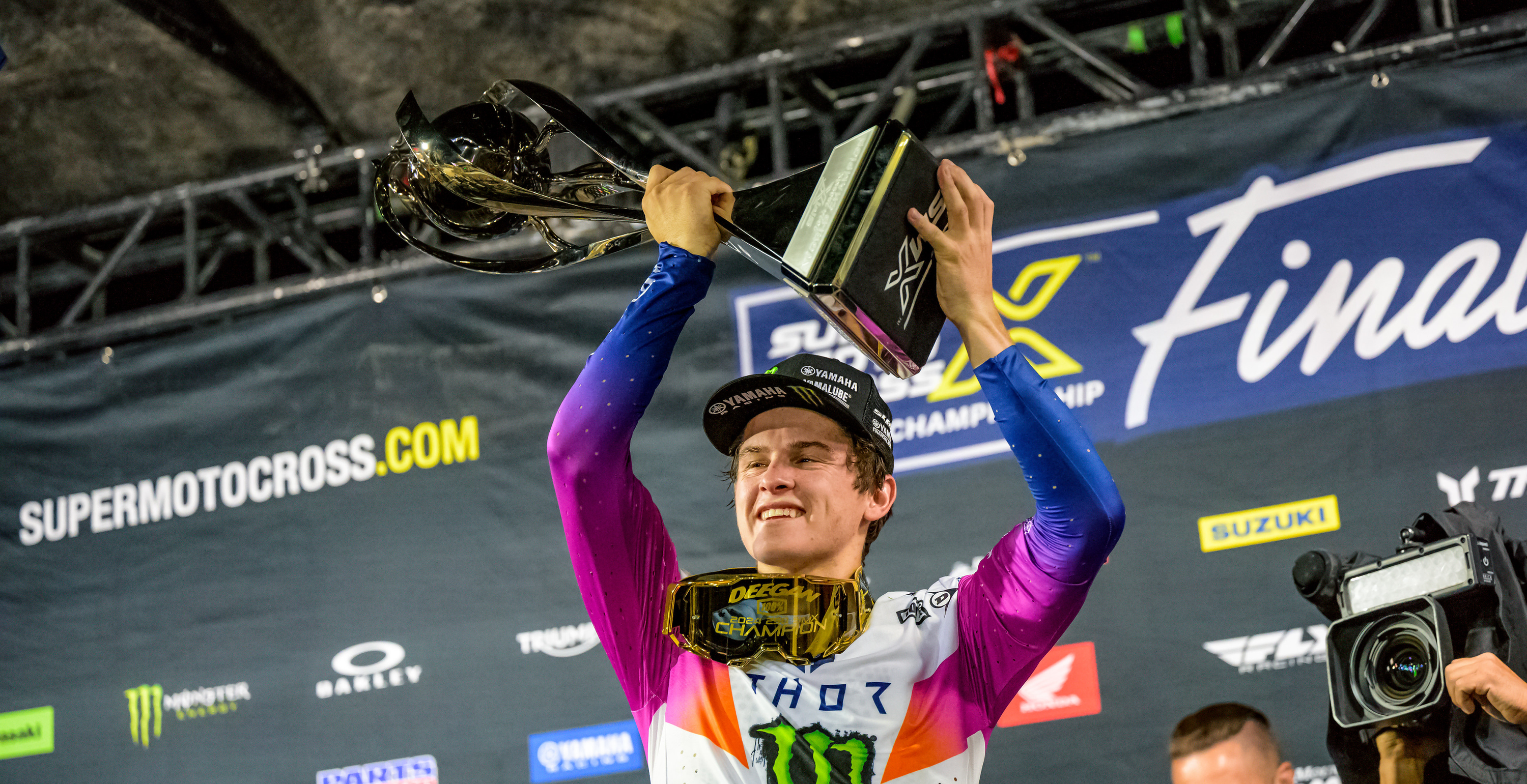 Motocross rider Haiden Deegan holding a trophy against a branded background