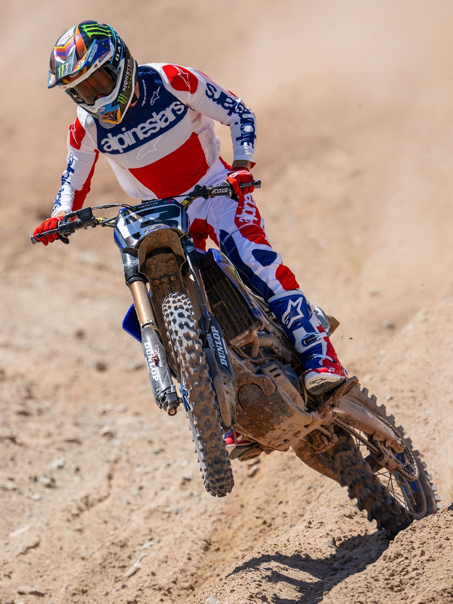 Motocross-Fahrer in Aktion auf einer Geländestrecke, trägt das Limited Edition Techstar Fortitude Trikot in Bright Red White and Blue, kombiniert mit farblich passender Rennhose und Stiefeln, mit markantem Alpinestars-Branding, professionelle Offroad-Rennbekleidung