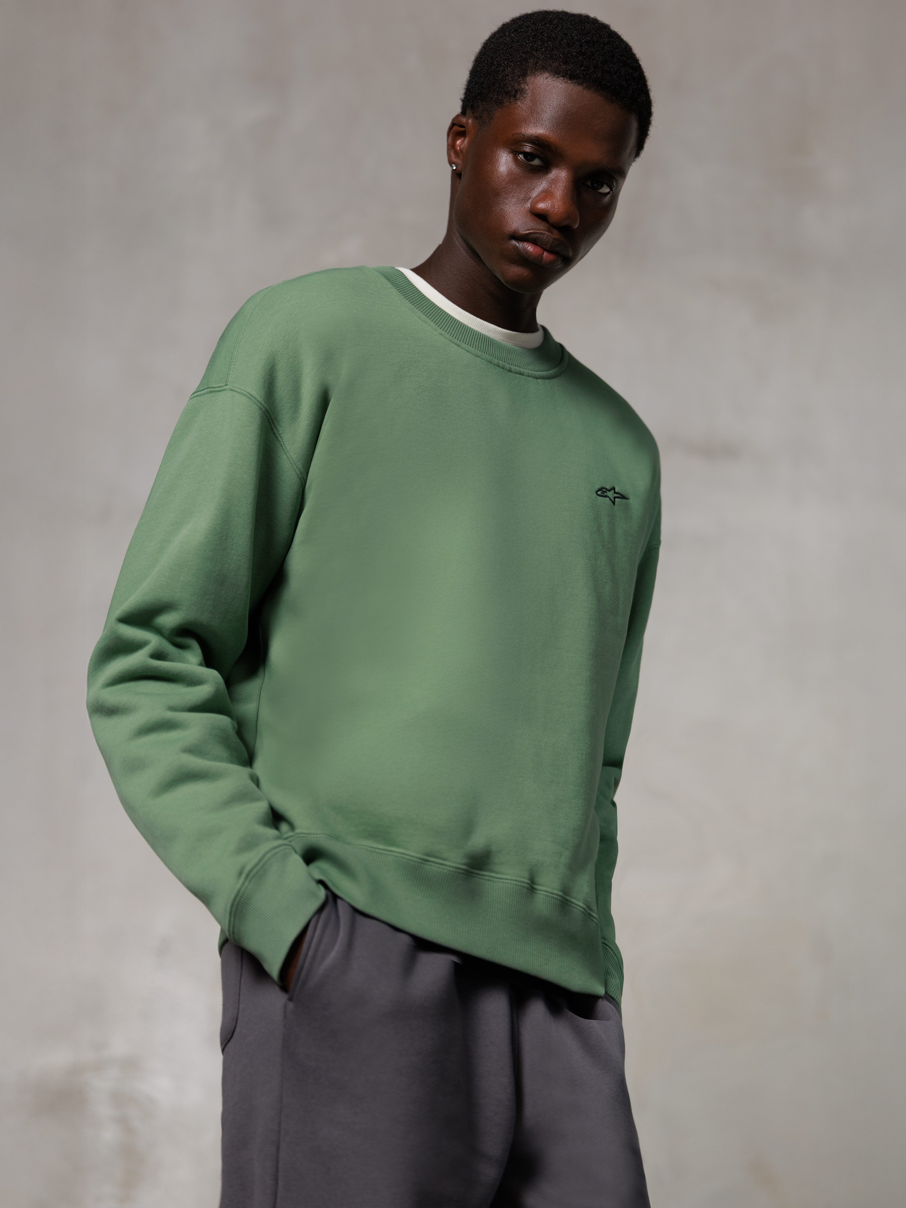 Alpinestars Essentials Ageless Crew, sweat-shirt à col rond, vert cactus, avec un petit logo Alpinestars noir sur la poitrine, porté par un mannequin avec un pantalon gris, style streetwear décontracté