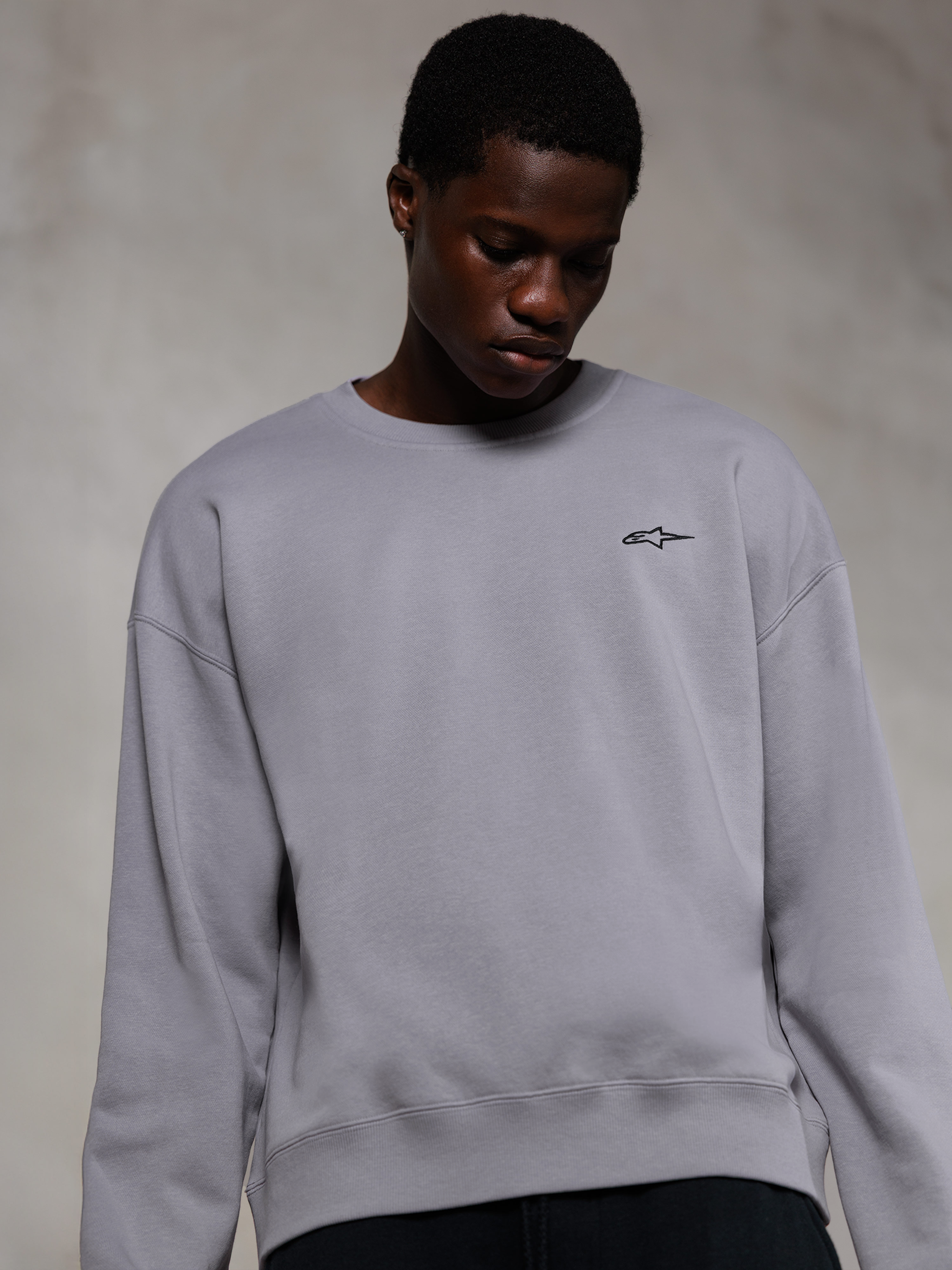 Alpinestars Essentials Ageless Crew, sweat-shirt à col rond premium argenté, avec un petit logo Alpinestars noir sur la poitrine, porté par un mannequin, style streetwear décontracté avec une texture polaire douce