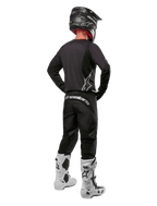 Alpinestars 2024 Fluid Graphite Gear Set, Motocross rider viewed from the back, graphite gray jersey and pants with silver Alpinestars branding, black helmet and white motocross boots, athletic fit gear for off-road riding
