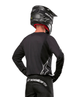 Alpinestars 2024 Fluid Graphite Gear Set, Motocross Jersey and Pants, Graphite and Silver, back view featuring silver branding on lower back and waist, worn with black carbon-effect helmet, lightweight poly-fabric design for off-road riding