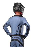 Alpinestars 2024 Fluid Lurv Trikot, Motocross-Trikot, Hellblau und Schwarz, Rückansicht des Fahrers mit großem Stern-Logo und Ärmel-Branding, getragen mit schwarzem Helm und passender Offroad-Hose, professionelle Rennbekleidung