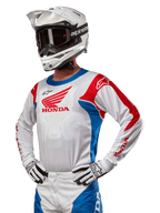 Motocross-Fahrer im Honda Racer Iconic Trikot in Weiß, Hellblau und Hellrot mit einem großen Honda-Flügel-Logo auf der Brust, kombiniert mit einem weißen Alpinestars-Helm und passenden weiß-schwarzen Handschuhen, abgestimmte Ausrüstung für Offroad-Performance