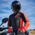Veste Alpinestars Viper Air V4 en rouge fluo et noir, portée par un motard sur une moto, avec un grand logo sur la poitrine et des panneaux en maille aérée, associée à un casque en fibre de carbone et des gants noirs, équipement de moto de route et de sport