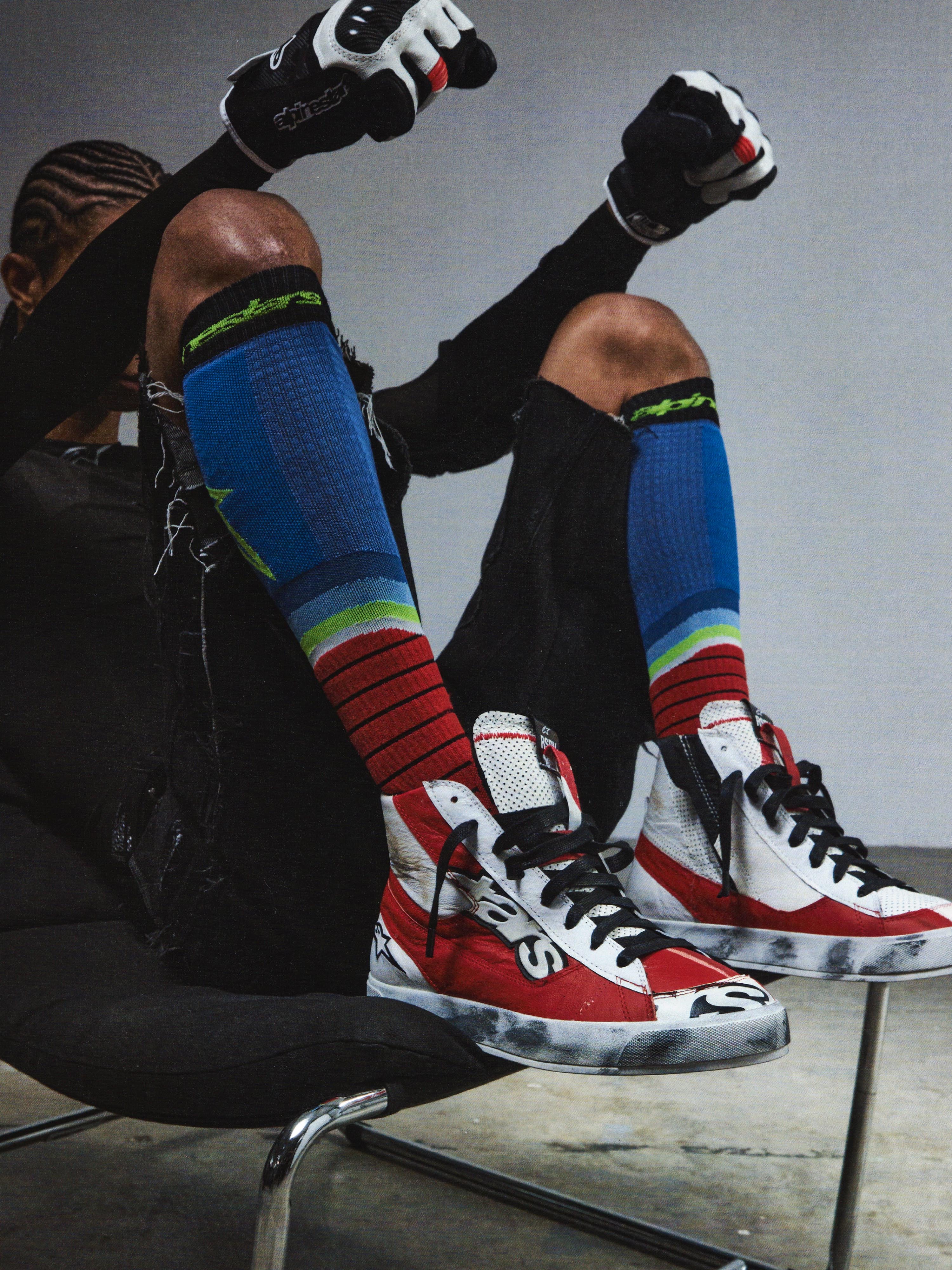 Alpinestars RSRV Legacy Shoe, chaussures streetwear premium, rouges, blanches et noires, portées avec chaussettes colorées à rayures bleues, vertes et rouges, style urbain lifestyle
