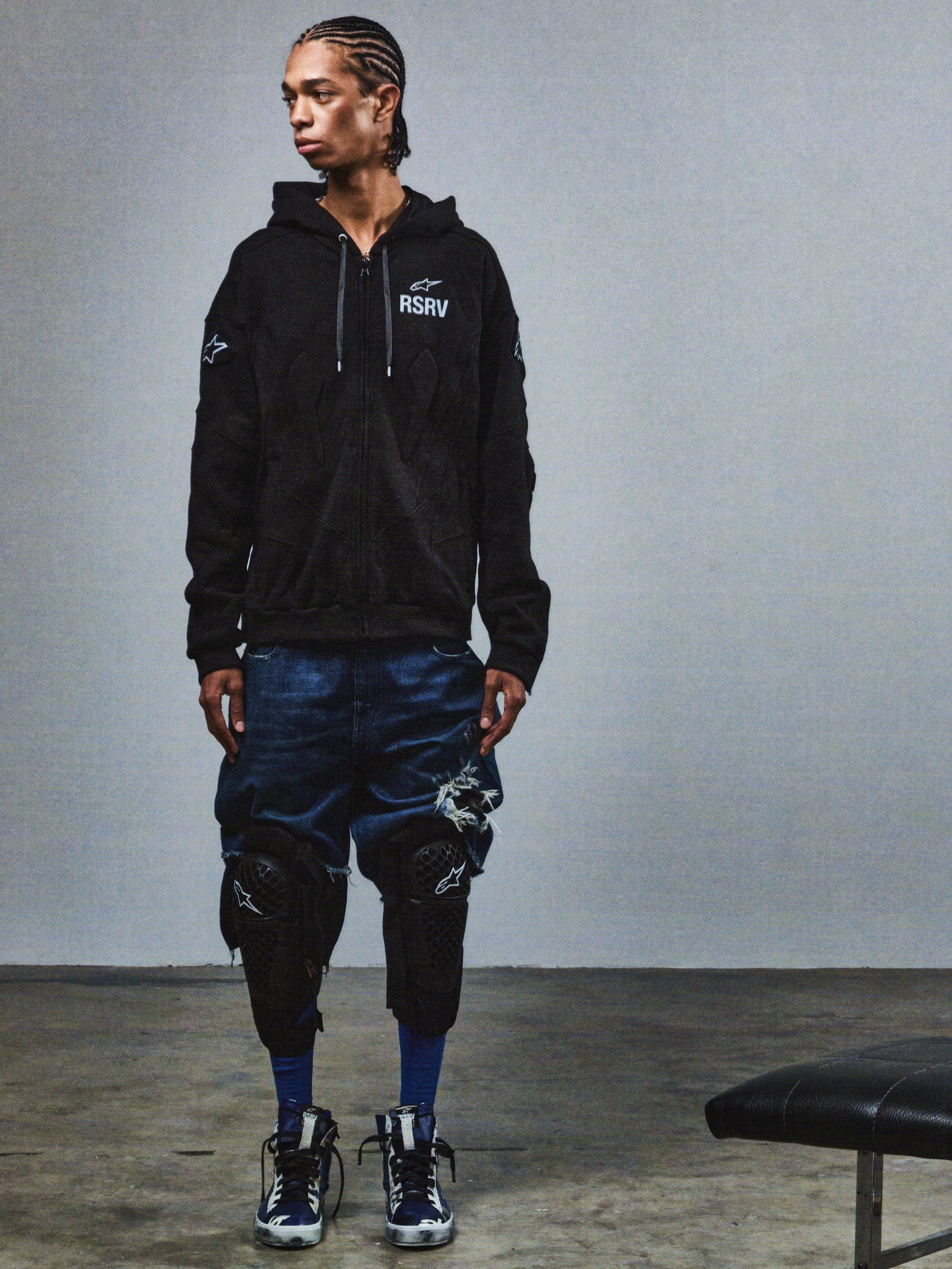 Alpinestars RSRV GP Hoodie, sweat à capuche noir unisexe avec logo RSRV et étoiles, style streetwear urbain, porté avec short en denim déchiré bleu et genouillères noires