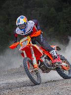 Pilote de motocross en action portant un maillot Alpinestars Pro-Dura noir, rouge vif et blanc, pilotant une moto orange sur un sentier poussiéreux, avec un pantalon noir et des bottes rouges et blanches