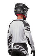 Alpinestars 2024 Racer Hana Trikot, Weiß und Schwarz, Rückansicht zeigt ergonomische Passform und markantes Ärmel-Branding, kombiniert mit einem schwarzen Motocross-Helm und dazu passender schwarz-weißer Hose, Hochleistungs-Rennausrüstung für Offroad-Fahrten
