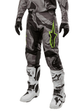 Alpinestars 2024 Racer Tactical Pants, pantalon de motocross, camouflage gris et noir, logo étoile vert citron, porté avec des bottes blanches et noires et des gants noirs, équipement de pilotage tout-terrain