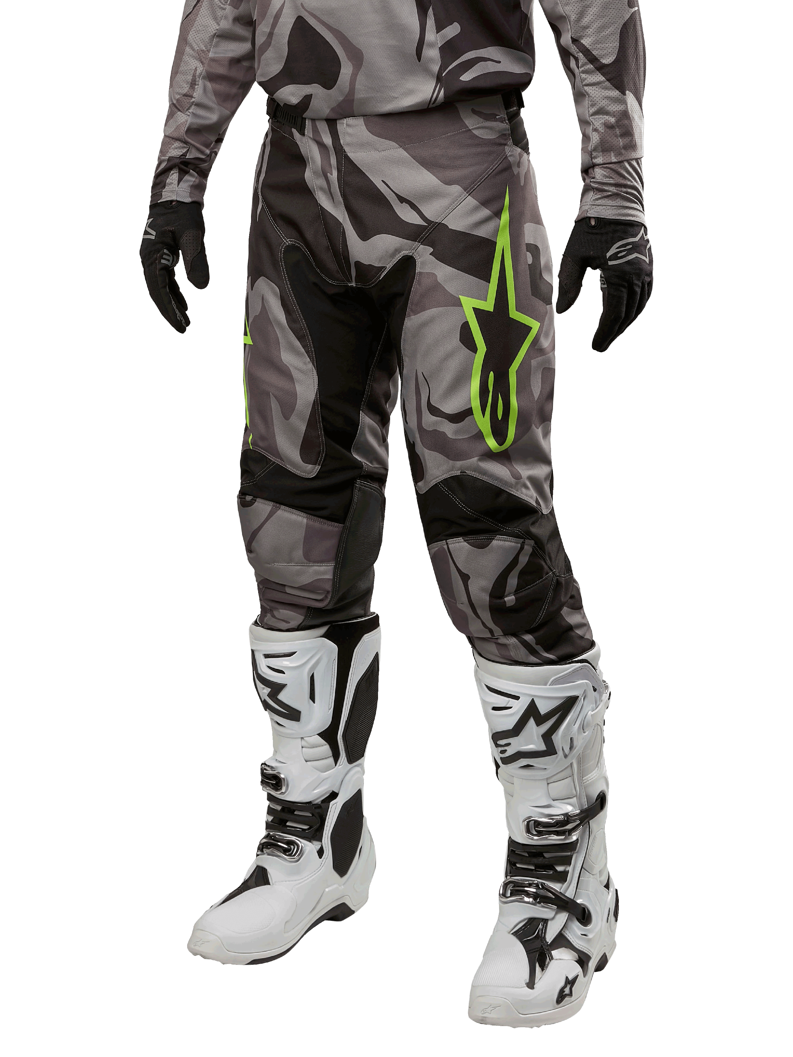 Alpinestars 2024 Racer Tactical Pants, pantalon de motocross, camouflage gris et noir, logo étoile vert citron, porté avec des bottes blanches et noires et des gants noirs, équipement de pilotage tout-terrain