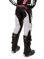 Pantalon Stella Fluid Femme 2024 Alpinestars, pantalon de motocross, noir et blanc, vue arrière montrant des panneaux de jambe blancs et un logo rose sur la taille, porté avec des bottes Tech 3 noires, équipement durable pour la course tout-terrain