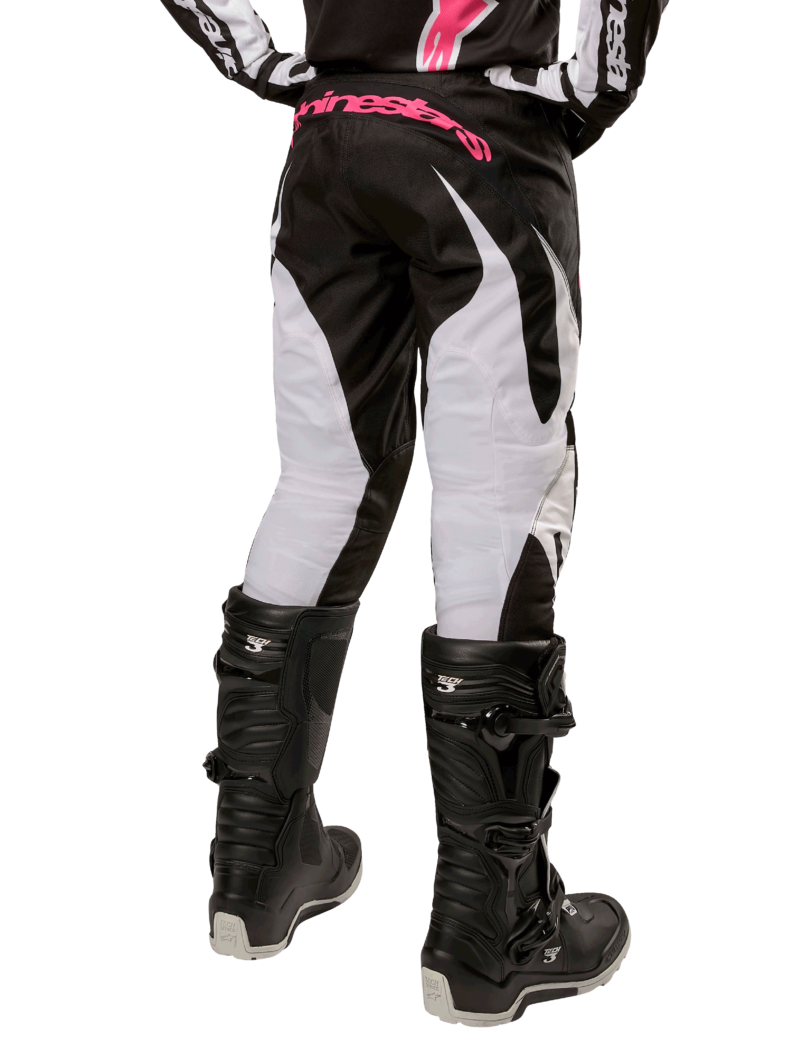 Pantalon Stella Fluid Femme 2024 Alpinestars, pantalon de motocross, noir et blanc, vue arrière montrant des panneaux de jambe blancs et un logo rose sur la taille, porté avec des bottes Tech 3 noires, équipement durable pour la course tout-terrain