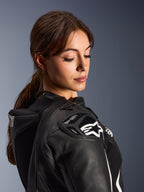 Vrouw die het Alpinestars Stella GP-R7 2-delig lederen pak draagt, close-up van de zwarte lederen schouder met DFS RR-bescherming en wit ster-logo, voorzien van de geïntegreerde aero-bult en geperforeerde details.