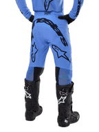 Pantalon Alpinestars Supertech Dade 2024, pantalon de motocross, bleu clair, vue arrière montrant un large marquage noir sur l'assise et les jambes, porté avec des bottes Alpinestars Tech 10 noires, coupe athlétique pour une performance tout-terrain professionnelle.