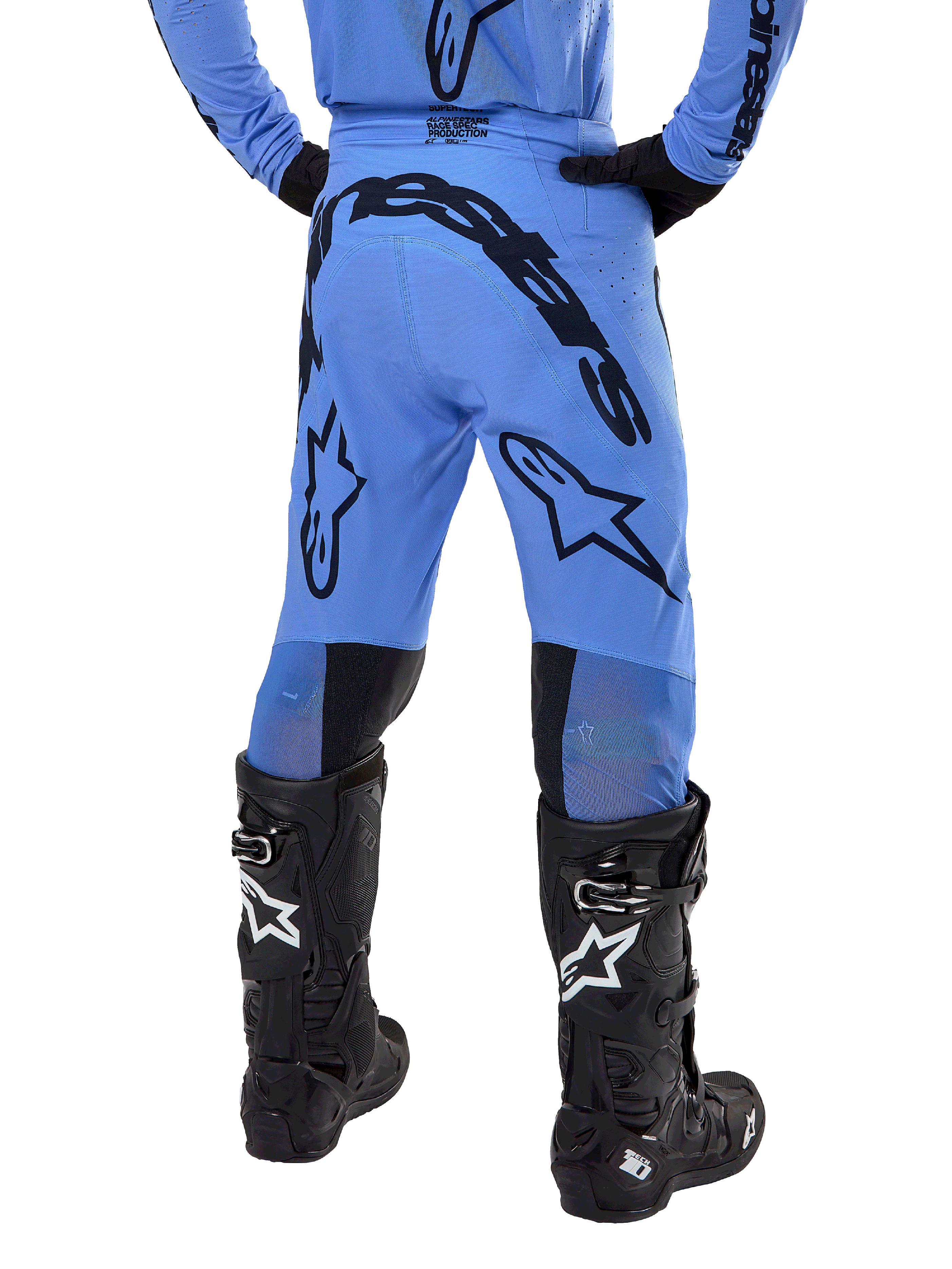 Pantalon Alpinestars Supertech Dade 2024, pantalon de motocross, bleu clair, vue arrière montrant un large marquage noir sur l'assise et les jambes, porté avec des bottes Alpinestars Tech 10 noires, coupe athlétique pour une performance tout-terrain professionnelle.