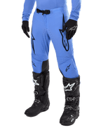 Alpinestars 2024 Supertech Dade Pants, pantalon de motocross, bleu clair avec logos graphiques noirs, avec perforations de ventilation et boucle magnétique à la taille, porté avec des bottes de pilotage techniques et des gants noirs, équipement de course tout-terrain professionnel
