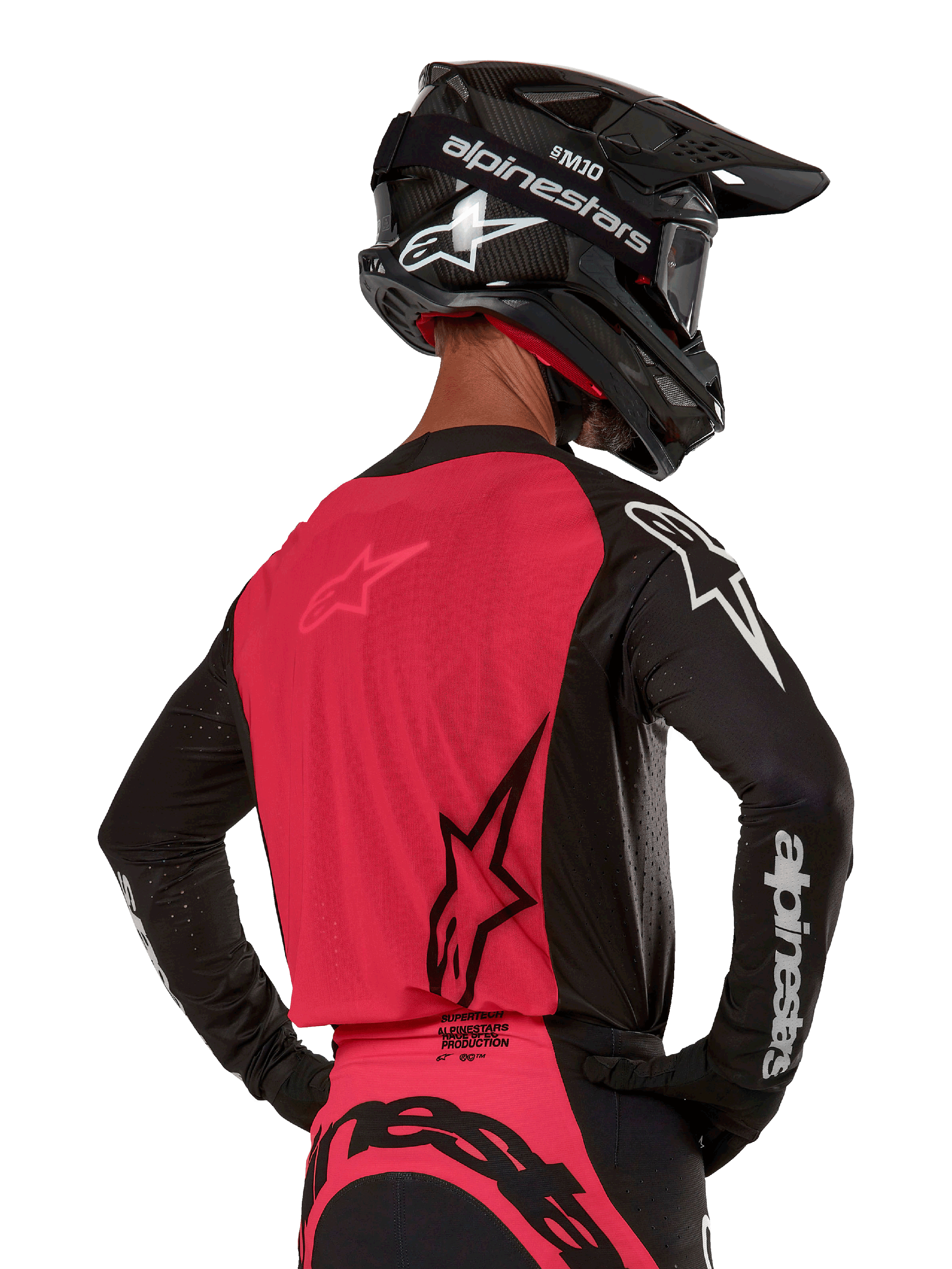 Alpinestars 2024 Supertech Ward Trikot, Motocross-Trikot, Schwarz und Red Berry, Rückansicht mit rotem Mesh-Einsatz und schwarzen Ärmeln mit weißem Branding, getragen mit schwarzem Carbon-Helm und Handschuhen, athletische Rennpassform für den Offroad-Einsatz