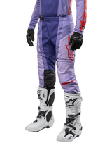 Alpinestars 2024 Techstar Ocuri Pants, pantalon de motocross, violet avec accents orange vif, logo rouge, porté avec des bottes blanches et noires et gants noirs, équipement de protection technique pour tout-terrain