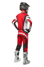 Alpinestars 2024 Techstar Ocuri Pants, pantalon de motocross, Mars Red White Black, vue arrière d'un pilote portant un équipement de course complet, incluant le maillot assorti, un casque noir et des bottes blanches et noires, mettant en avant le logo Alpinestars et la construction en tissu durable.