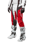 Alpinestars 2024 Techstar Ocuri Pants, pantalon de motocross, rouge Mars, blanc et noir, porté avec un maillot blanc et noir assorti, des gants noirs et des bottes de course blanches à boucles, équipement de protection technique sur fond blanc
