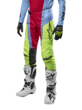 Alpinestars 2024 Techstar Ocuri crossbroek, motorcross broek, lichtblauw, bessenrood en neongeel, gedragen met bijpassende uitrusting en witte laarzen, voorzien van opvallende Astars-branding en een prestatiegerichte racepasvorm.