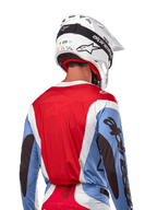 Alpinestars Maillot Techstar Ocuri 2024, maillot de motocross, bleu clair, rouge Mars et blanc, vue arrière d'un pilote portant un casque blanc assorti et des lunettes noires, avec marquage noir audacieux sur les manches et coupe ergonomique pour la performance tout-terrain