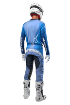 Motocross-Fahrer von hinten in Alpinestars 2024 Techstar Pneuma Hose, Dunkelblau und Hellblau, kombiniert mit passendem blauem Trikot, weißem Helm, weißen Handschuhen und weißen Stiefeln, markantes Alpinestars-Branding auf Gesäß und Ärmeln