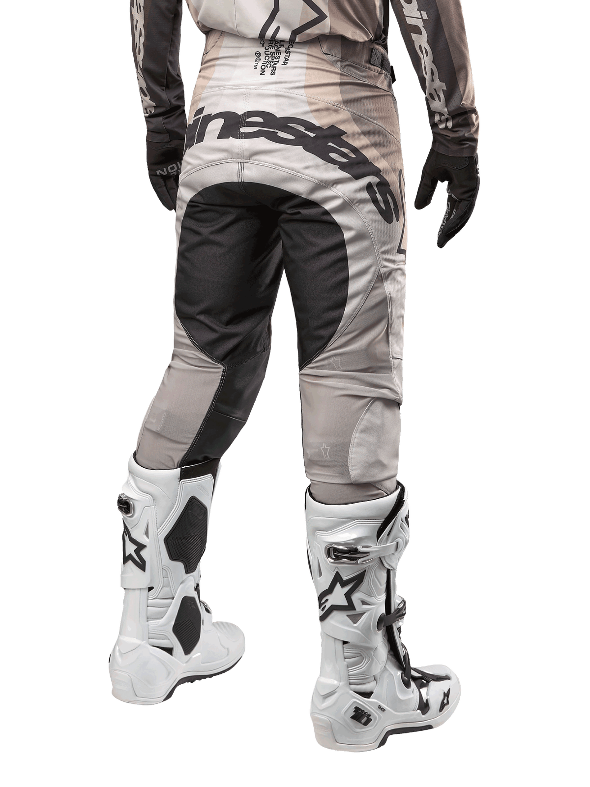 Pantalon Alpinestars Techstar Pneuma 2024, pantalon de motocross, sable foncé et gris poussière de fer, vue arrière à partir de la taille, logo Alpinestars noir sur l'assise, porté avec des bottes de motocross blanches et noires et des gants noirs, conception durable à coupe de course pour la compétition tout-terrain