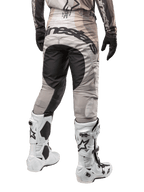 Pantalon Alpinestars Techstar Pneuma 2024, pantalon de motocross, sable foncé et gris poussière de fer, vue arrière à partir de la taille, logo Alpinestars noir sur l'assise, porté avec des bottes de motocross blanches et noires et des gants noirs, conception durable à coupe de course pour la compétition tout-terrain