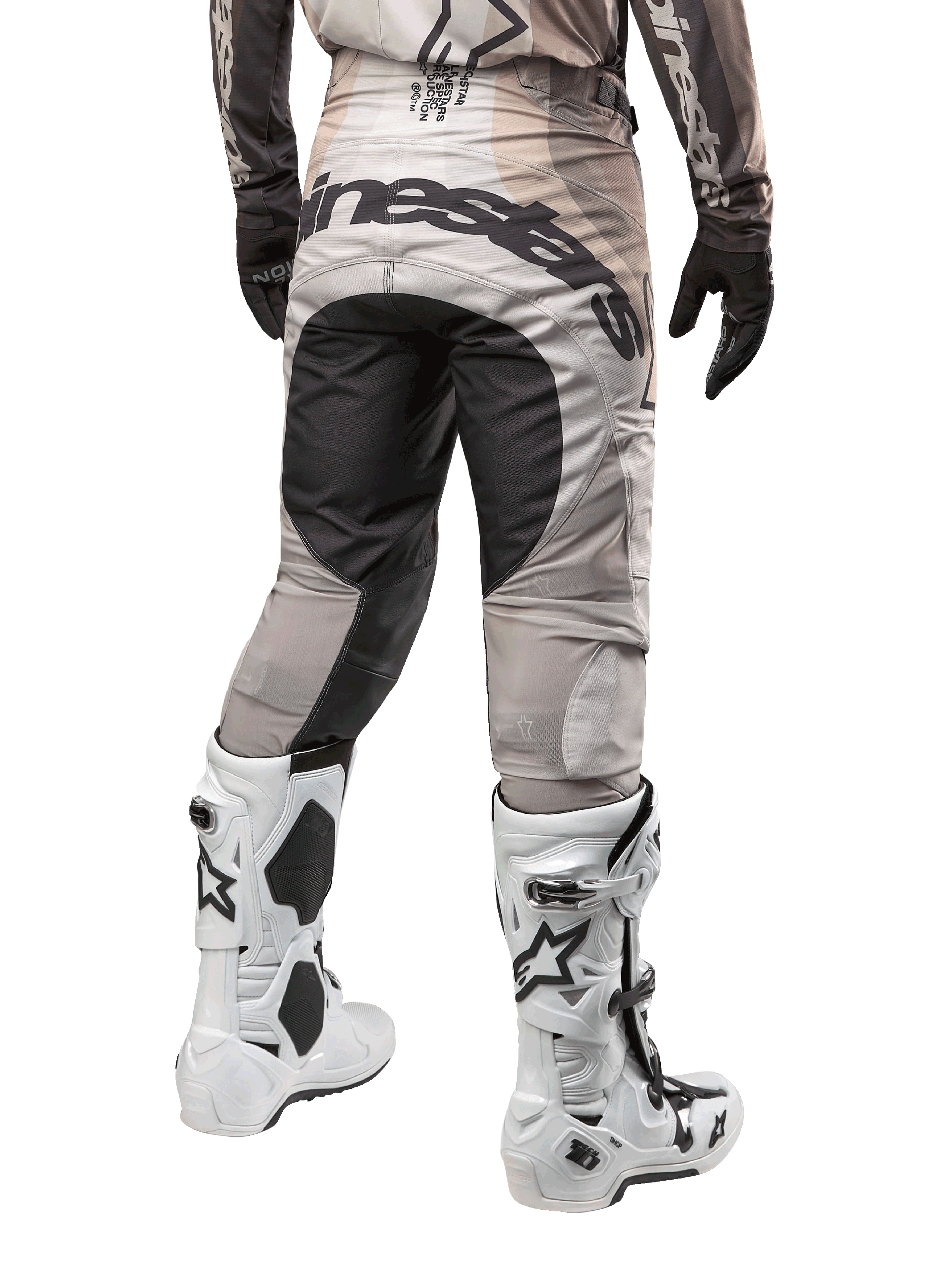 Pantalon Alpinestars Techstar Pneuma 2024, pantalon de motocross, sable foncé et gris poussière de fer, vue arrière à partir de la taille, logo Alpinestars noir sur l'assise, porté avec des bottes de motocross blanches et noires et des gants noirs, conception durable à coupe de course pour la compétition tout-terrain