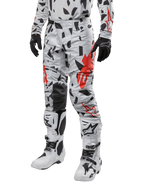 Alpinestars Pantalon Techstar Rantera 2024, pantalon de motocross, camouflage gris brume avec motifs abstraits noirs et rouges, porté avec un maillot assorti, des gants noirs et des bottes de motocross blanches, conçu pour la course tout-terrain haute performance