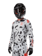 Alpinestars 2024 Techstar Rantera Trikot, Motocross-Trikot, Haze Gray Camo mit schwarzen abstrakten Mustern und roten Akzenten, Langarm-Design getragen mit passendem schwarzem Helm und Handschuhen, technische Offroad-Rennausrüstung