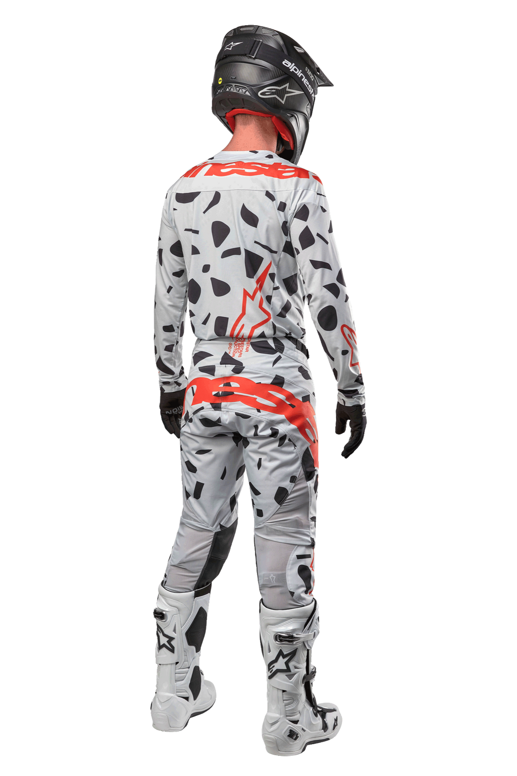 Pilote de motocross vu de dos portant le pantalon Alpinestars Techstar Rantera 2024, camouflage gris avec taches noires et logos rouges, maillot assorti, casque noir et bottes blanches, tenue de course tout-terrain complète