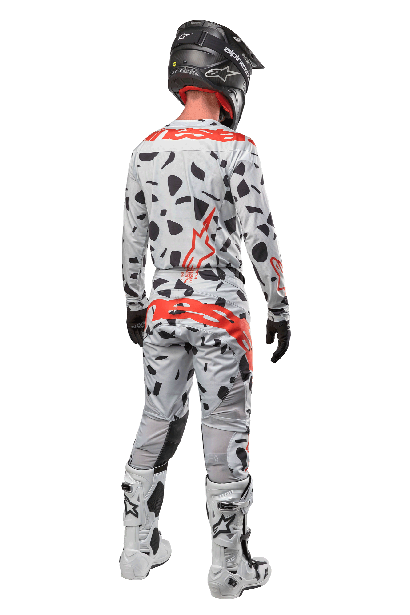 Pilote de motocross vu de dos portant le pantalon Alpinestars Techstar Rantera 2024, camouflage gris avec taches noires et logos rouges, maillot assorti, casque noir et bottes blanches, tenue de course tout-terrain complète
