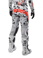 Pantalon Alpinestars Techstar Rantera 2024, pantalon de motocross, Haze Gray Camo avec motifs de camouflage noirs et un grand logo Alpinestars rouge sur l'assise, vue arrière porté avec des bottes blanches et un équipement de course assorti