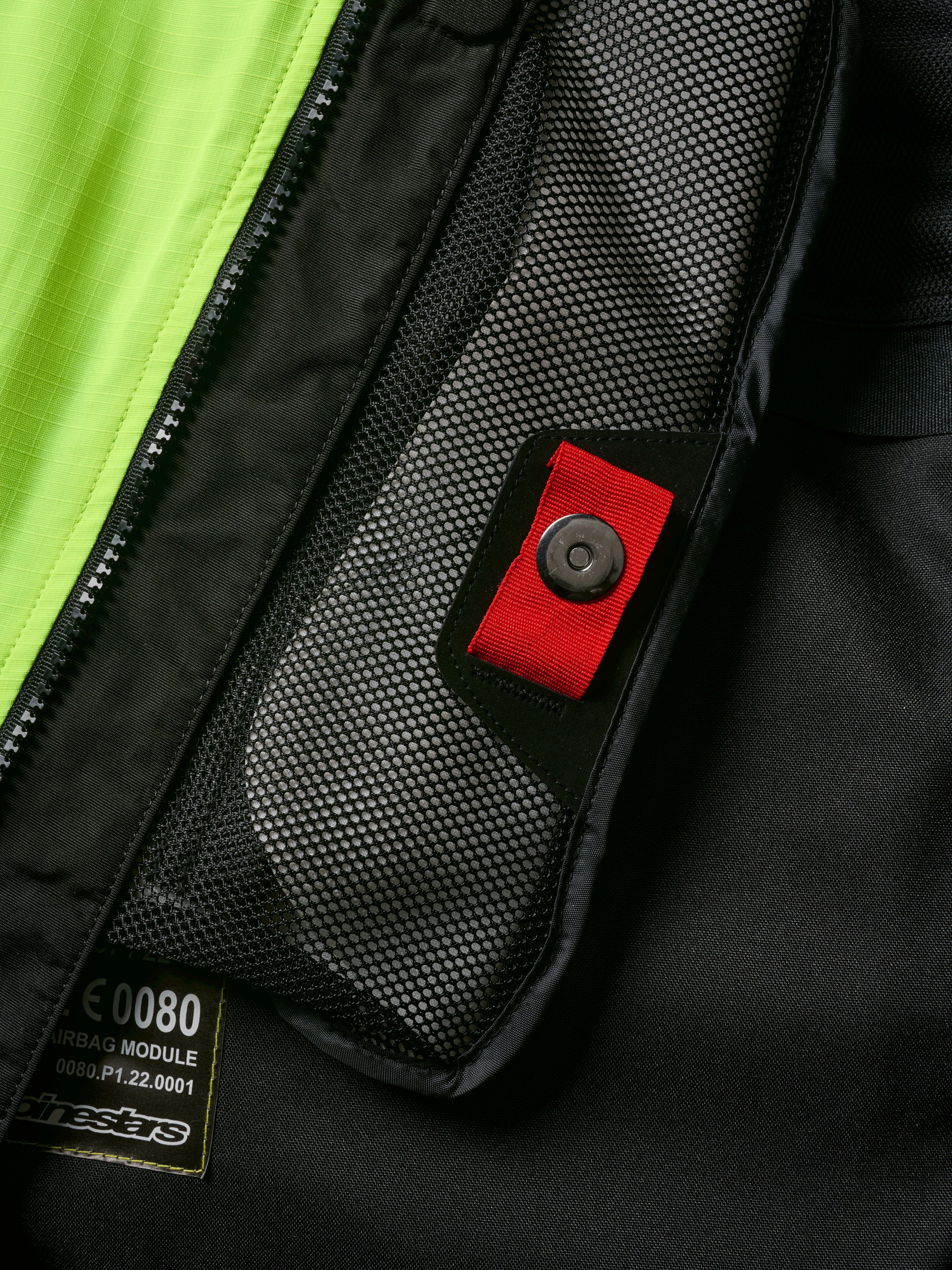 Alpinestars Tech-Air® 3 V2 System detail, close-up of internal mesh pocket with red pull tab and snap fastener, vibrant yellow fluo panel, black textile construction showing airbag module label and zipper