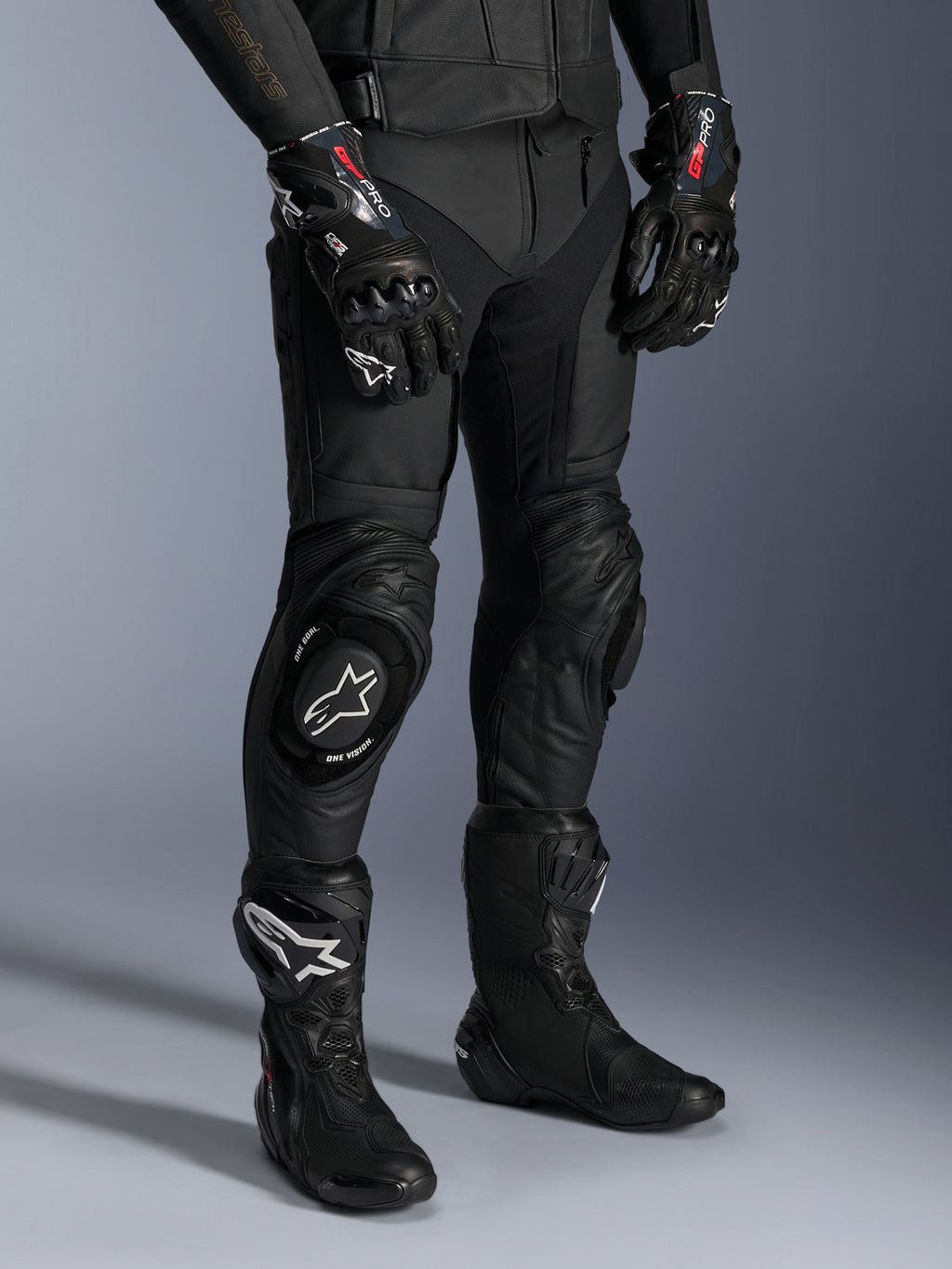 Missile V3 Leren Broek, zwarte motorracebroek, gedragen met bijpassende GP Pro-handschoenen en technische racelaarzen, premium lederen constructie met witte logo-knieschuivers, professionele race-esthetiek voor circuit- en weggebruik
