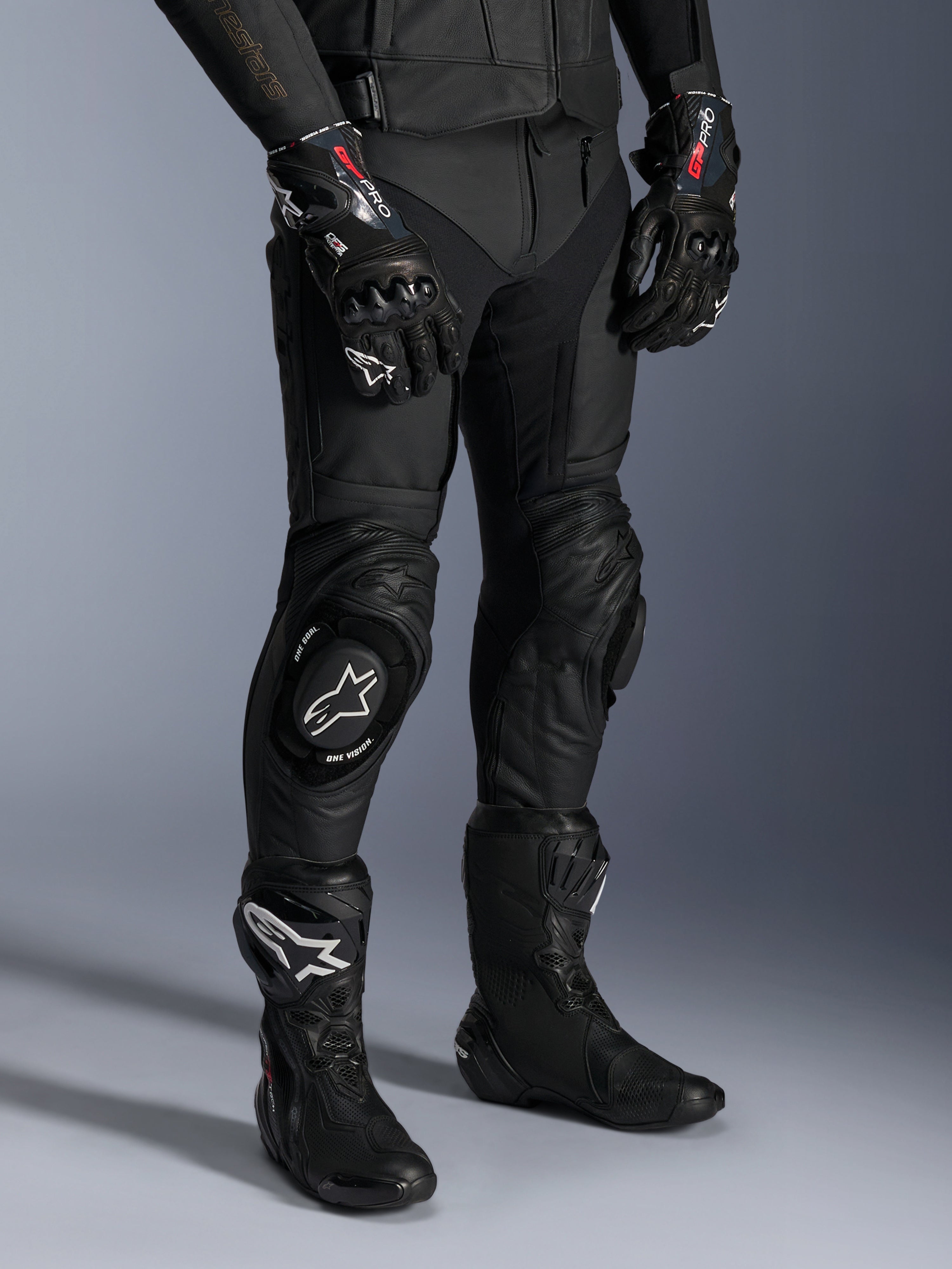 Missile V3 Leren Broek, zwarte motorracebroek, gedragen met bijpassende GP Pro-handschoenen en technische racelaarzen, premium lederen constructie met witte logo-knieschuivers, professionele race-esthetiek voor circuit- en weggebruik