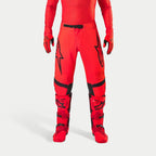 Pantalon Alpinestars Supertech Ember LE, pantalon de motocross, rouge fluo et rouge vif avec des détails noirs, arborant des logos d'étoile noirs sur les cuisses, une boucle de taille et des empiècements aux genoux noirs, porté avec des bottes et des gants rouges assortis pour une tenue de course coordonnée.