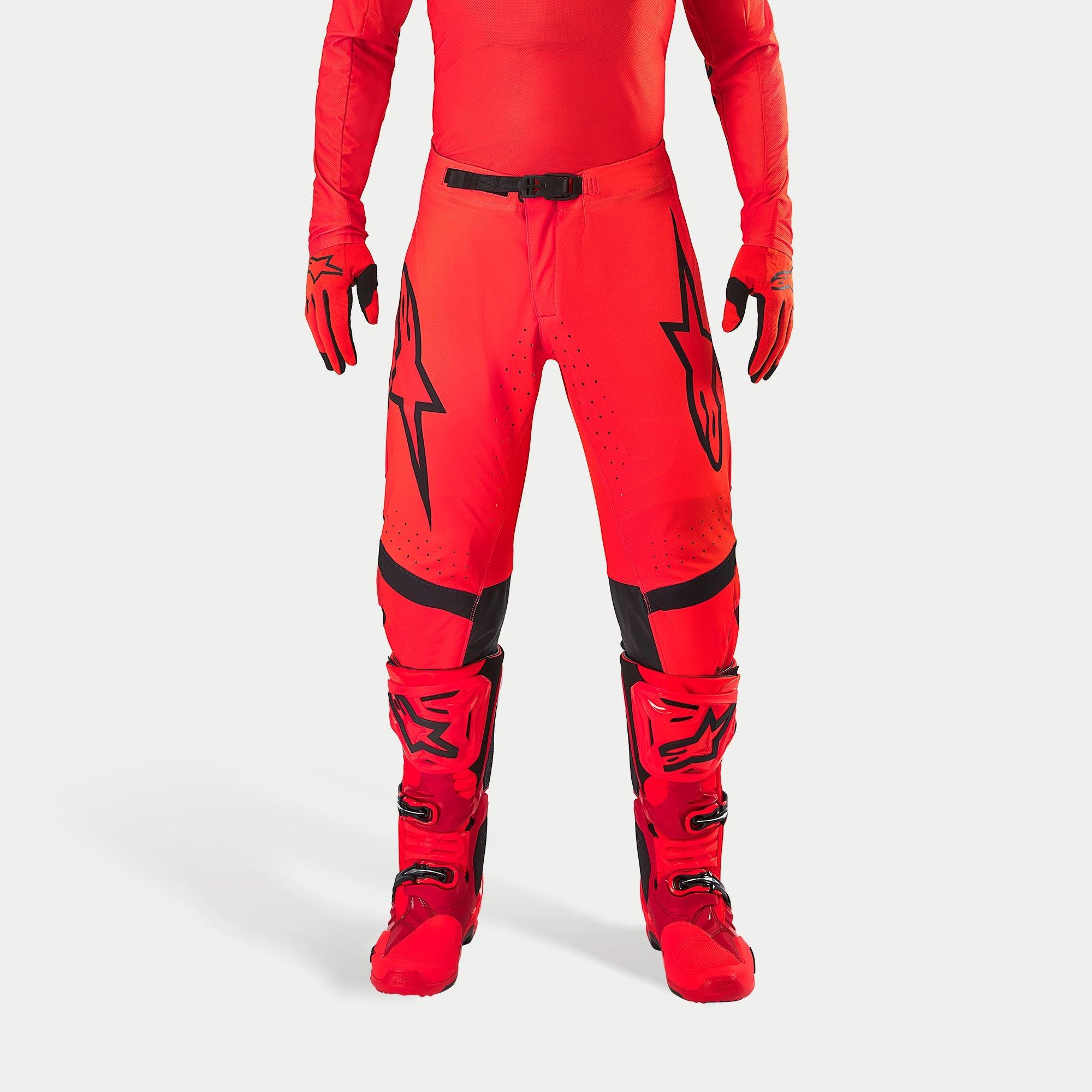 Pantalon Alpinestars Supertech Ember LE, pantalon de motocross, rouge fluo et rouge vif avec des détails noirs, arborant des logos d'étoile noirs sur les cuisses, une boucle de taille et des empiècements aux genoux noirs, porté avec des bottes et des gants rouges assortis pour une tenue de course coordonnée.