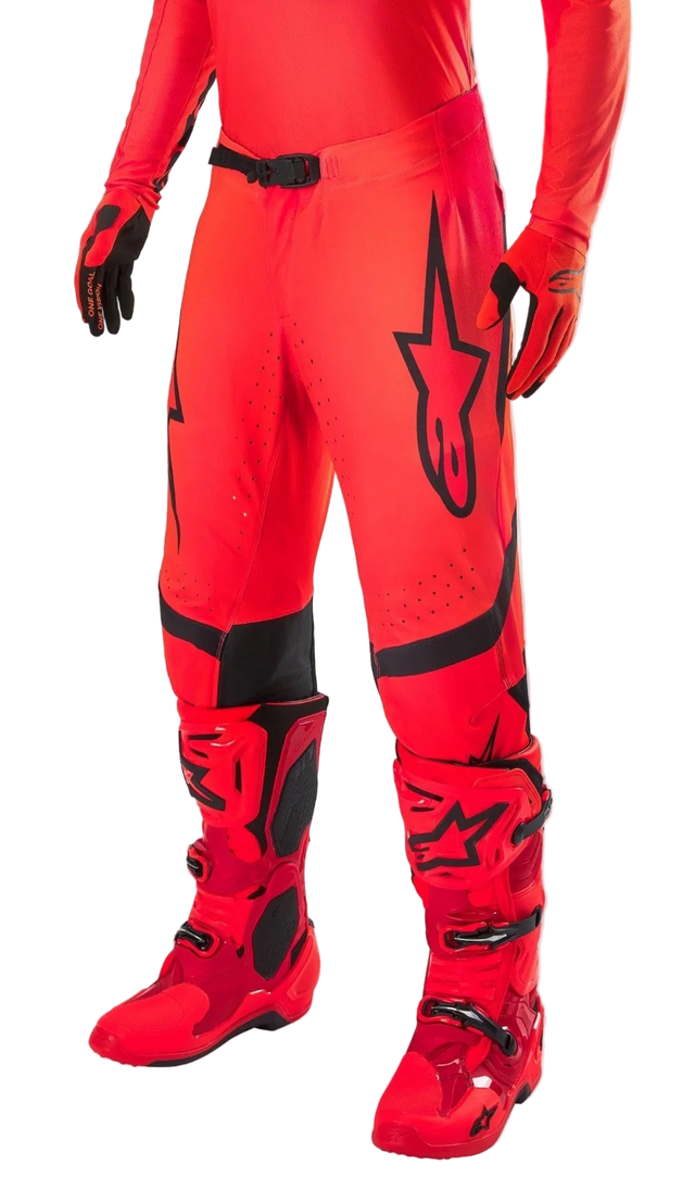 Alpinestars Supertech Ember LE Motocross Pants, Red Fluo and Bright Red with Black accents, worn with matching red racing boots and gloves, featuring a prominent black star logo on the leg, secure waist buckle, and perforated zones for ventilation.