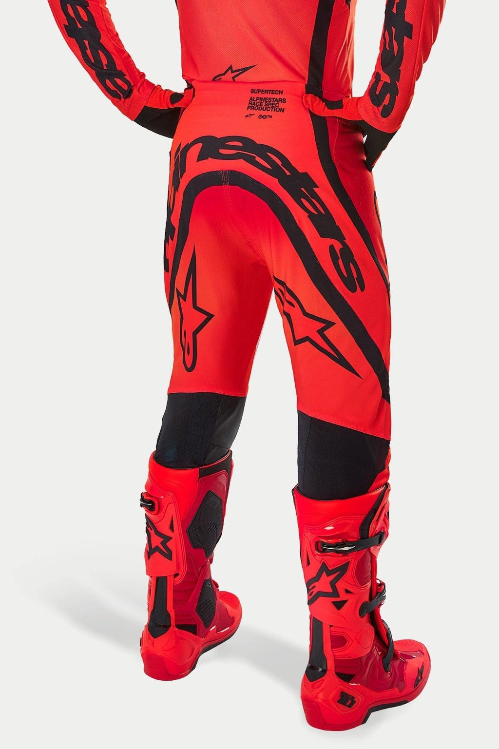 Alpinestars Supertech Ember LE Pants, pantalon de motocross, rouge fluo, rouge vif et noir, vue arrière présentant un large marquage noir sur l'assise et des logos étoiles, porté avec des bottes de motocross rouges assorties, équipement de course professionnel pour la performance tout-terrain