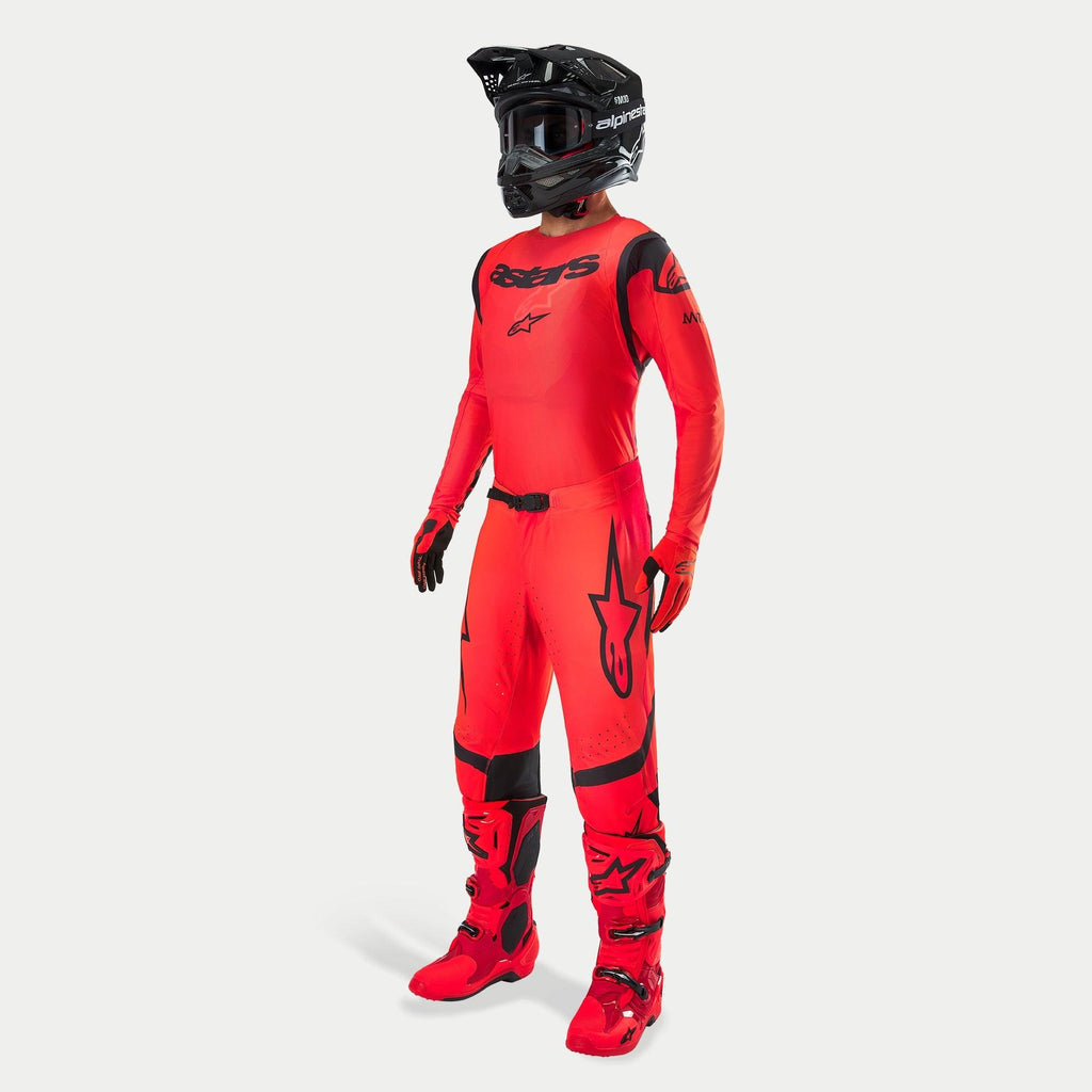 Pilote de motocross portant une tenue de course complète, maillot et pantalon Supertech Ember LE en rouge fluo et noir, casque noir avec lunettes, bottes et gants assortis rouge et noir, tenue professionnelle coordonnée pour la course tout-terrain